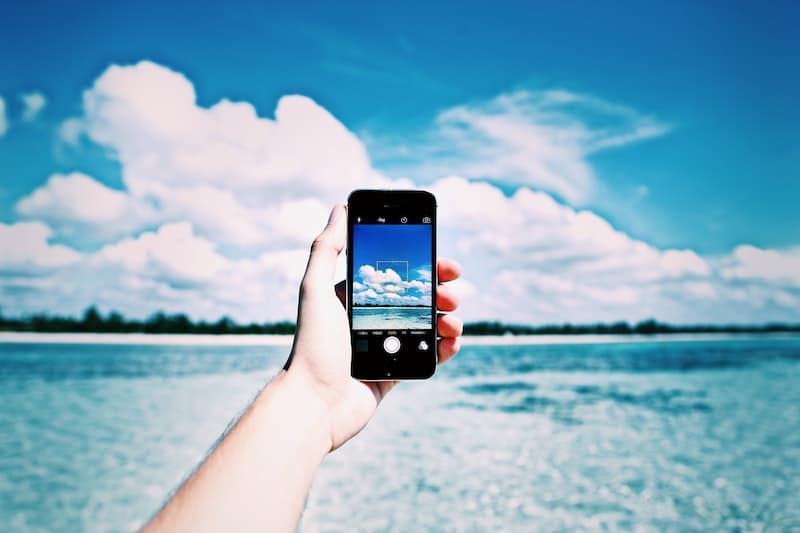 Person holding Google Pixel 4 capturing sky and clouds over water.