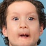 Child with curly hair and blue eyes looking surprised, against a blue background.