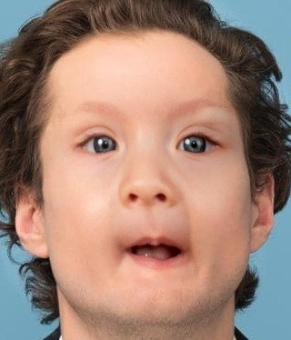 Child with curly hair and blue eyes looking surprised, against a blue background.