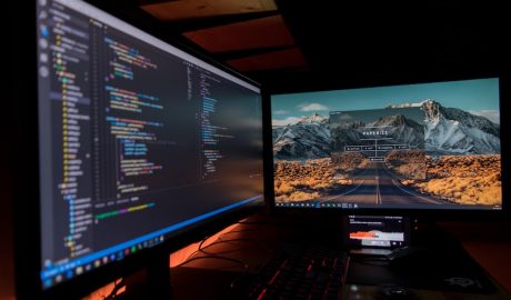 Dual monitor setup displaying code and mountain landscape background for software development and te.