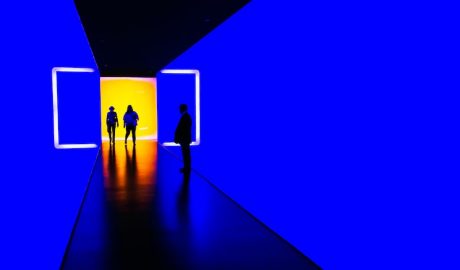 People exploring an immersive digital art installation with vibrant blue and yellow lighting.