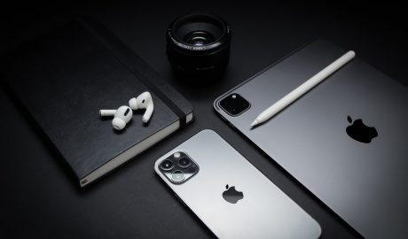 An iphone next to a lense and a macbook. dark image, almost black and white