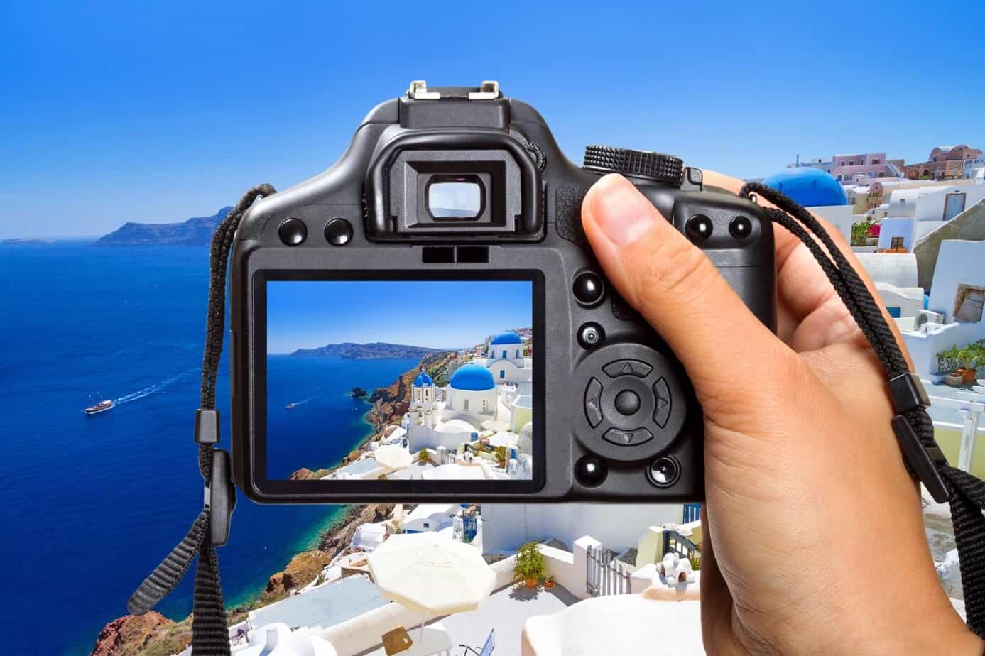 Photographer taking picture of Santorini's white buildings and blue domes with a digital camera.