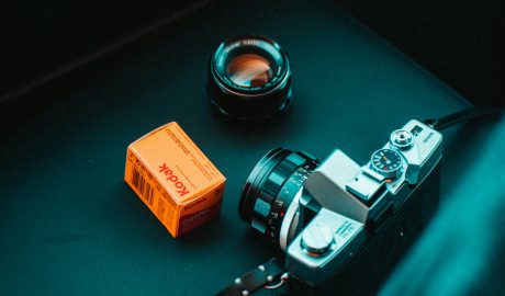 Vintage film camera with lens and Kodak film box on dark surface.