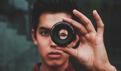 Young man holding camera lens, exploring authenticity in photography.