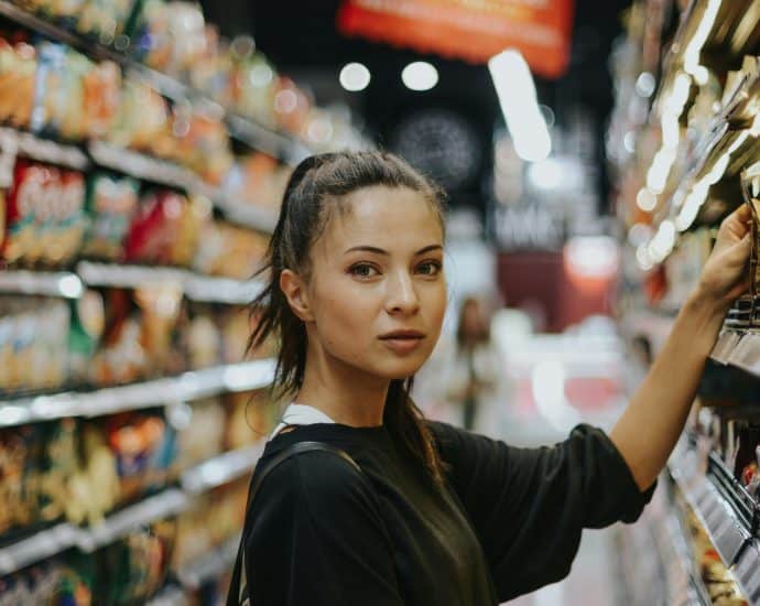 Young woman shopping for snacks in a grocery store aisle.