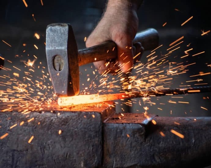Blacksmith hammer striking glowing heated metal with sparks.